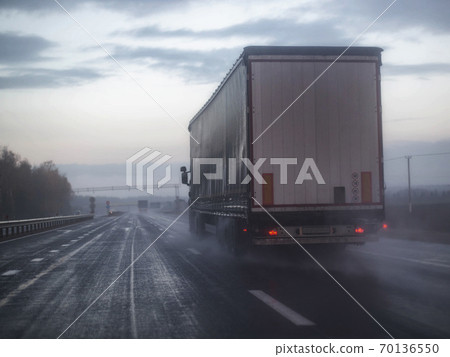 A truck wagon rides on a highway with poor visibility where it rains and fog, background. Bad Road Safety Concept, copy space A truck wagon rides on a highway with poor visibility where it rains and fog, background. Bad Road Safety Concept, copy space 70136550