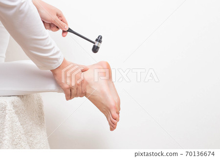 A neurologist doctor checks the Achilles reflex with a neurological hammer. Checking the tibial nerve and the presence of an intervertebral hernia of the spine, copy space A neurologist doctor checks the Achilles reflex with a neurological hammer. Checking the tibial nerve and the presence of an intervertebral hernia of the spine, copy space 70136674
