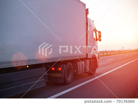 a truck with an isotherm semitrailer transports cargo along the highway against the backdrop of an evening sunset. Concept of delivery of goods, cargo transportation, copy space for text 70136866
