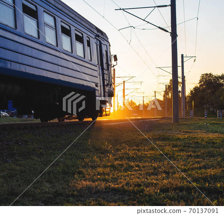 Passenger train for transporting people moves on the railroad against the background of sunset, copy space for text Passenger train for transporting people moves on the railroad against the background of sunset, copy space for text 70137091