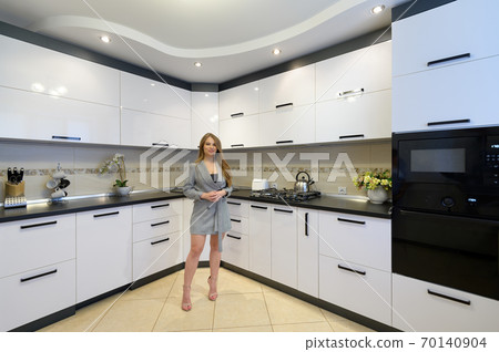 Young woman at luxury modern white kitchen interior in modern style Young woman at luxury modern white kitchen interior in modern style 70140904