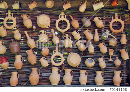 Rustic vintage clay jugs, pots and mugs hanging on wicker wall. 70141168
