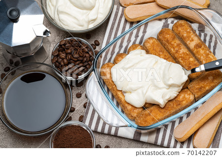 tiramisu dessert cooking - Traditional Italian Savoiardi ladyfingers Biscuits and cream in glass baking dish, coffe maker on concrete background tiramisu dessert cooking - Traditional Italian Savoiardi ladyfingers Biscuits and cream in glass baking dish, coffe maker on concrete background 70142207
