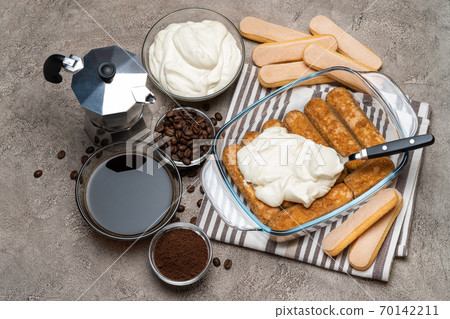 tiramisu dessert cooking - Traditional Italian Savoiardi ladyfingers Biscuits and cream in glass baking dish, coffe maker on concrete background 70142211