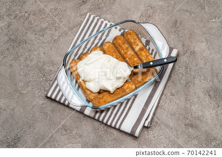 tiramisu dessert cooking - Traditional Italian Savoiardi ladyfingers Biscuits and cream in glass baking dish on concrete background tiramisu dessert cooking - Traditional Italian Savoiardi ladyfingers Biscuits and cream in glass baking dish on concrete background 70142241
