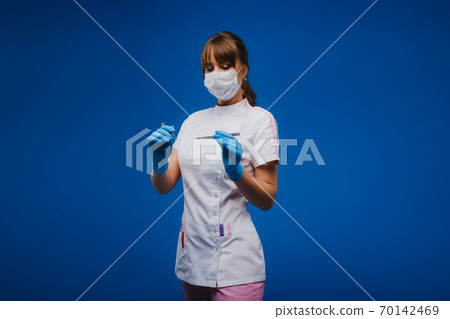 An attractive young female doctor holds a scalpel and looks directly at the camera. Concept of healthcare, treatment and surgery. Portrait of a medical practitioner on a blue background An attractive young female doctor holds a scalpel and looks directly at the camera. Concept of healthcare, treatment and surgery. Portrait of a medical practitioner on a blue background 70142469