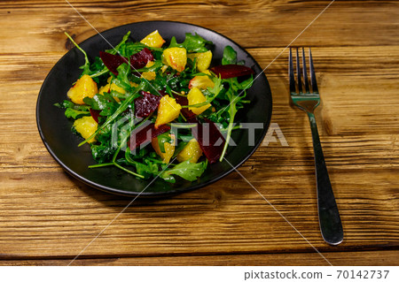 Tasty salad of fresh arugula, beetroot and oranges on wooden table. Healthy food or vegetarian concept Tasty salad of fresh arugula, beetroot and oranges on wooden table. Healthy food or vegetarian concept 70142737
