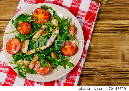 Tasty salad of fried chicken breast, fresh arugula and cherry tomatoes on wooden table. Top view 70142739