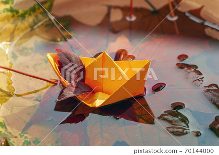 Origami paper boat and scenic fallen leaves in a water. Concept of bright fall Origami paper boat and scenic fallen leaves in a water. Concept of bright fall 70144000