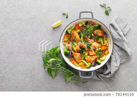 Chicken drumsticks roasted with vegetables in cast iron pan on kitchen table, top down view Chicken drumsticks roasted with vegetables in cast iron pan on kitchen table, top down view 70144110