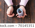 female hands in handcuffs hold twisted money on a dark wooden background 70145351