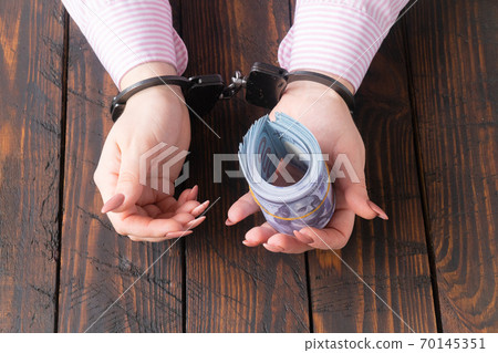 female hands in handcuffs hold twisted money on a dark wooden background female hands in handcuffs hold twisted money on a dark wooden background 70145351