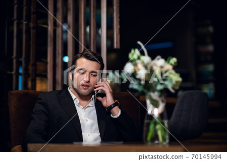 handsome man talking on the phone, sitting at a bar table handsome man talking on the phone, sitting at a bar table 70145994