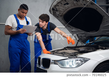 Repairer consults with a colleague about a car repair Repairer consults with a colleague about a car repair 70146025