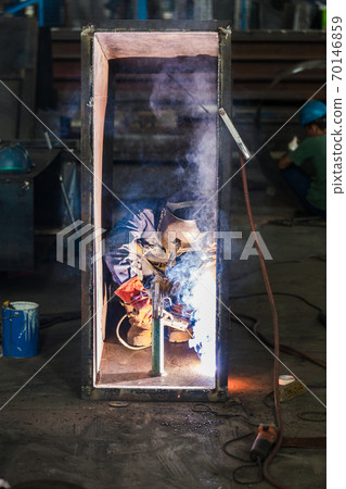 Blue-collar worker welding in the interior of a factory Blue-collar worker welding in the interior of a factory 70146859