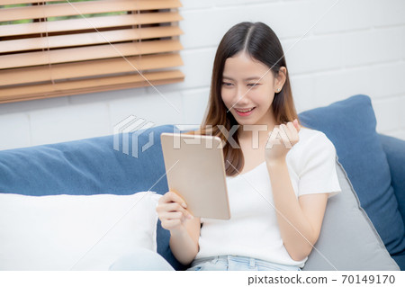 Young attractive asian woman resting using browsing tablet computer on sofa at home. 70149170