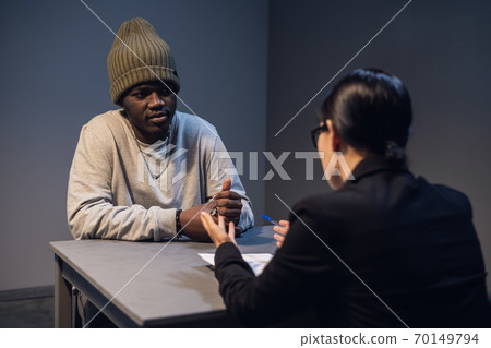 A beautiful girl investigator in an elegant suit asks a black criminal to cooperate with the investigation and sign a confession. 70149794