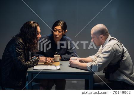 At the police station, two officers are interrogating the captured criminal 70149902