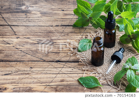 Fragrant mint essential oil in dark glass bubbles, aromatherapy oil natural organic cosmetic on rustic wood background. Fragrant mint essential oil in dark glass bubbles, aromatherapy oil natural organic cosmetic on rustic wood background. 70154163