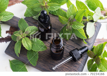 Fragrant mint essential oil in dark glass bubbles, aromatherapy oil natural organic cosmetic on rustic wood background. Fragrant mint essential oil in dark glass bubbles, aromatherapy oil natural organic cosmetic on rustic wood background. 70154166