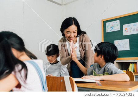 Young Asian teacher giving boy high five in school, success, achievement, happiness. Asia school boy with young woman in class 70154322