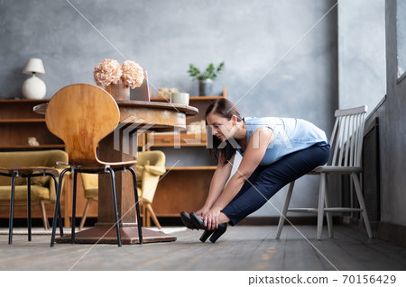 Caucasian young woman doing paschimottanasana sitting on chair. Caucasian young woman doing paschimottanasana sitting on chair. 70156429