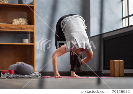 Woman working out indoors standing in Uttanasana during online lesson. 70156623