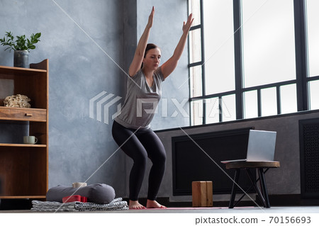 Caucasian woman doing Utkatasana, Chair Pose using block at home Caucasian woman doing Utkatasana, Chair Pose using block at home 70156693