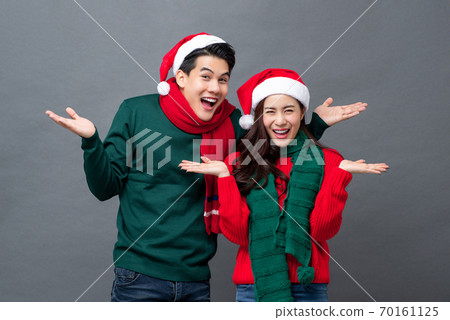 Smiling Asian couple wearing colorful Christmas attire doing open hands gesture Smiling Asian couple wearing colorful Christmas attire doing open hands gesture 70161125