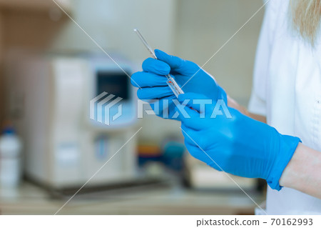 doctor's hand in rubber blue glove holding transparent syringe with closed cap doctor's hand in rubber blue glove holding transparent syringe with closed cap 70162993
