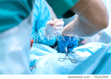 Closeup surgeon hand in glove apply clamp. Group of surgeons in operating room with surgery equipment. Medical background 70162994