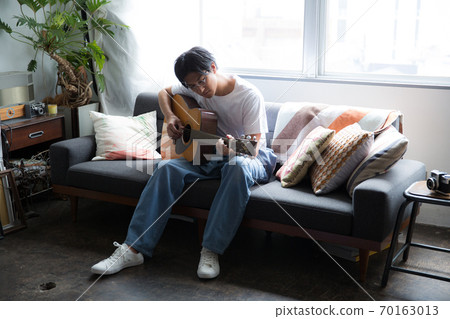 A cool man playing the guitar in the room A cool man playing the guitar in the room 70163013