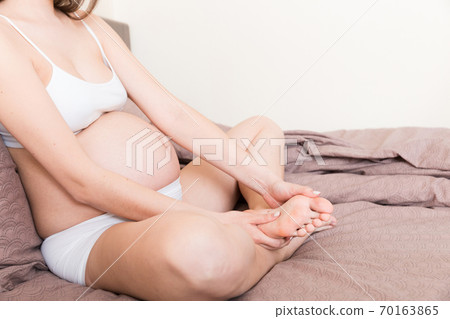 Pretty pregnant woman hands massaging leg sitting on bed 70163865