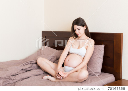 Pretty pregnant woman hands massaging leg sitting on bed 70163866