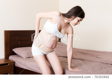 closeup pregnant woman dresses bandage on belly at home on bed. Orthopedic abdominal support belt closeup pregnant woman dresses bandage on belly at home on bed. Orthopedic abdominal support belt 70163882
