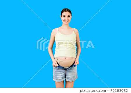 Portrait of pregnant woman wearing pregnancy bandage at blue background with copy space. Orthopedic abdominal support belt concept Portrait of pregnant woman wearing pregnancy bandage at blue background with copy space. Orthopedic abdominal support belt concept 70165082
