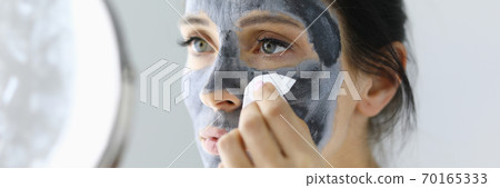 Woman looks in mirror and rinses off cosmetic mask. 70165333