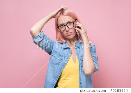 woman in glasses talking on the phone being puzzled. woman in glasses talking on the phone being puzzled. 70165334
