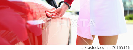 Woman stands next to red car hand on doorknob. 70165346