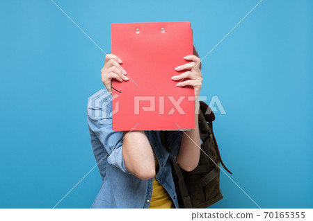 Caucasian student hiding her face behind a book, isolated on blue background. 70165355
