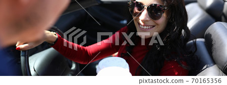 Woman sits in car smiling holds coffee in her hands next to man. Woman sits in car smiling holds coffee in her hands next to man. 70165356