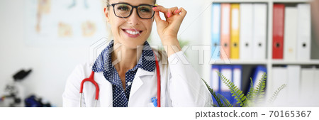 Woman doctor with glasses smiling at workplace in medical office 70165367