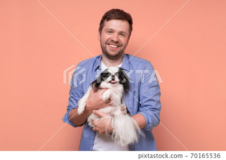 Happy caucasian man holding and comforting cute pet dogs japanese chin 70165536