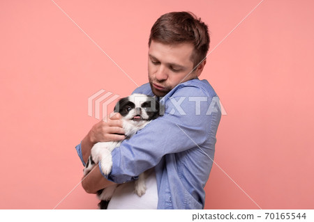 Happy caucasian man holding and comforting cute pet dogs japanese chin Happy caucasian man holding and comforting cute pet dogs japanese chin 70165544