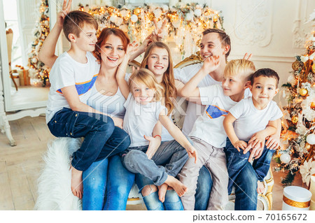 Happy family mother father five children relax playing near Christmas tree on Christmas eve at home. Mom dad daughter son in light room with winter decoration. Christmas New Year time for celebration 70165672