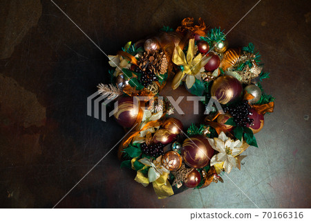 Christmas wreath on brown background with copyspace. Wreath decorated with balls and bows of gold and brown, with green leaves Christmas wreath on brown background with copyspace. Wreath decorated with balls and bows of gold and brown, with green leaves 70166316
