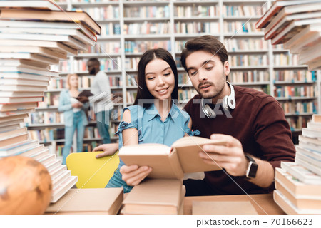 Girl with a guy reading a new book in the library. Girl with a guy reading a new book in the library. 70166623