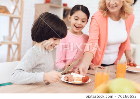 Grandmother puts plate for her grandson with food. 70166652