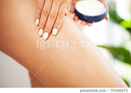 Woman applying body cream on her leg in bedroom, closeup Woman applying body cream on her leg in bedroom, closeup 70166875