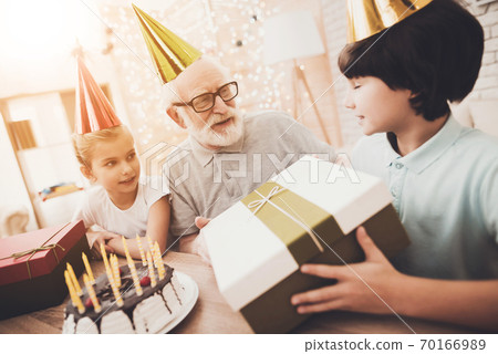 Grandfather with glasses looks at boy with a gift. Grandfather with glasses looks at boy with a gift. 70166989